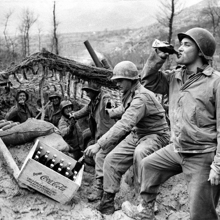 WWII troops pause to enjoy a Coca-Cola in an active combat zone. The staff of the Coca-Cola bottling plant established in Saipan. National W