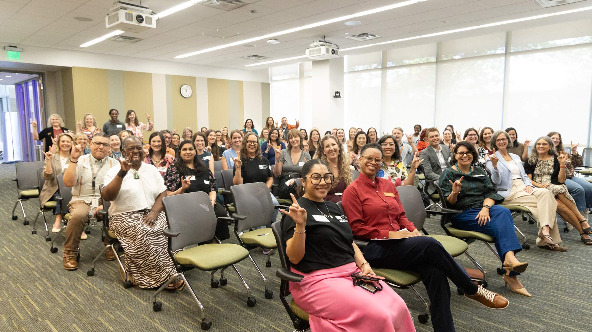 Attendees at the UT 2026 Research Administrator Day celebration smile and hold up Hook em signs in a conference room.