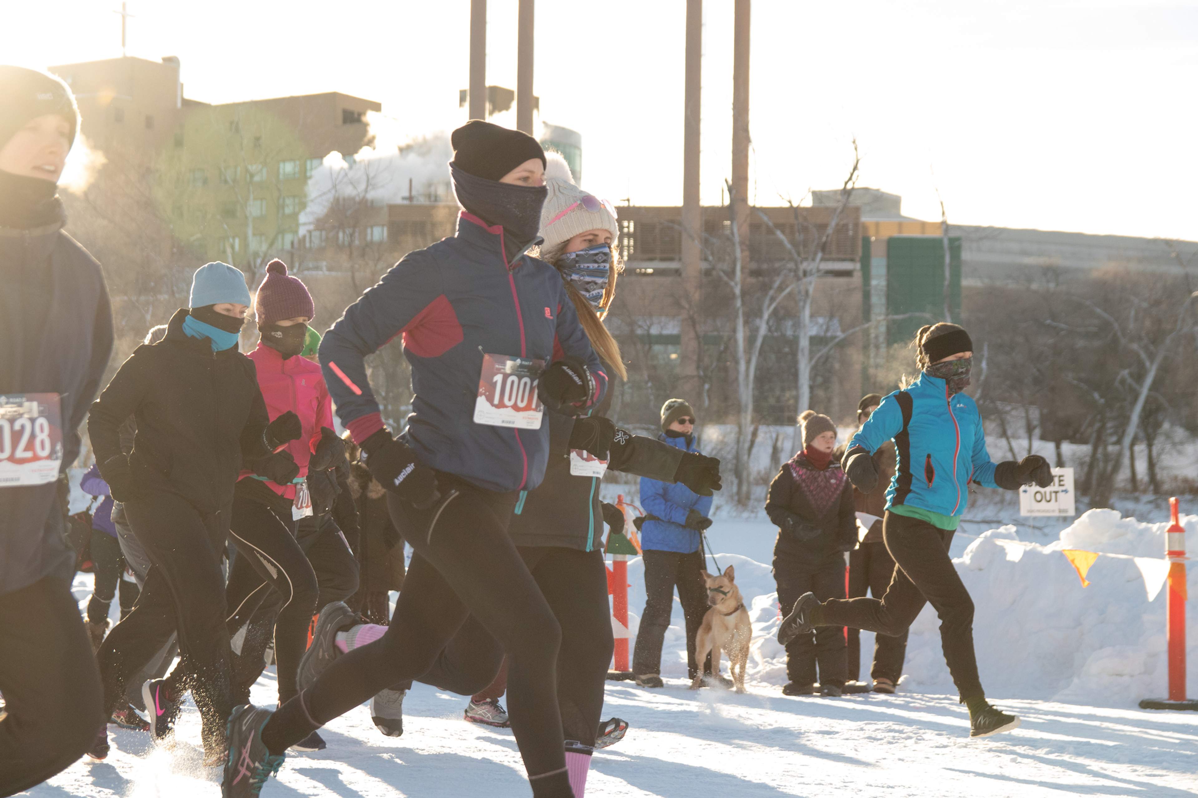 A crowd of people in jackets and winter running gear run through the snow.