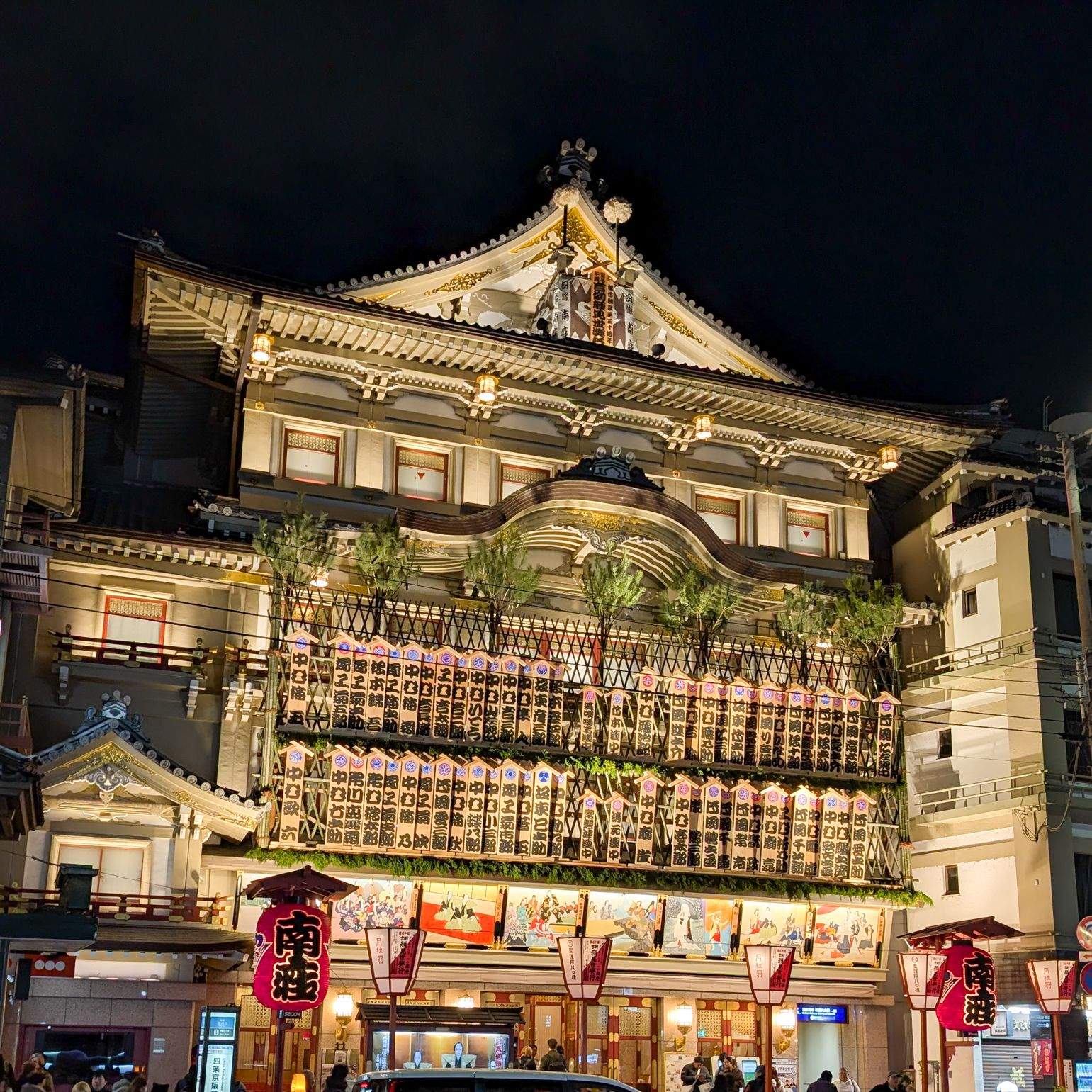 The illuminated Minamiza Theatre in Kyoto at night, covered in traditional kabuki signage and red lanterns.