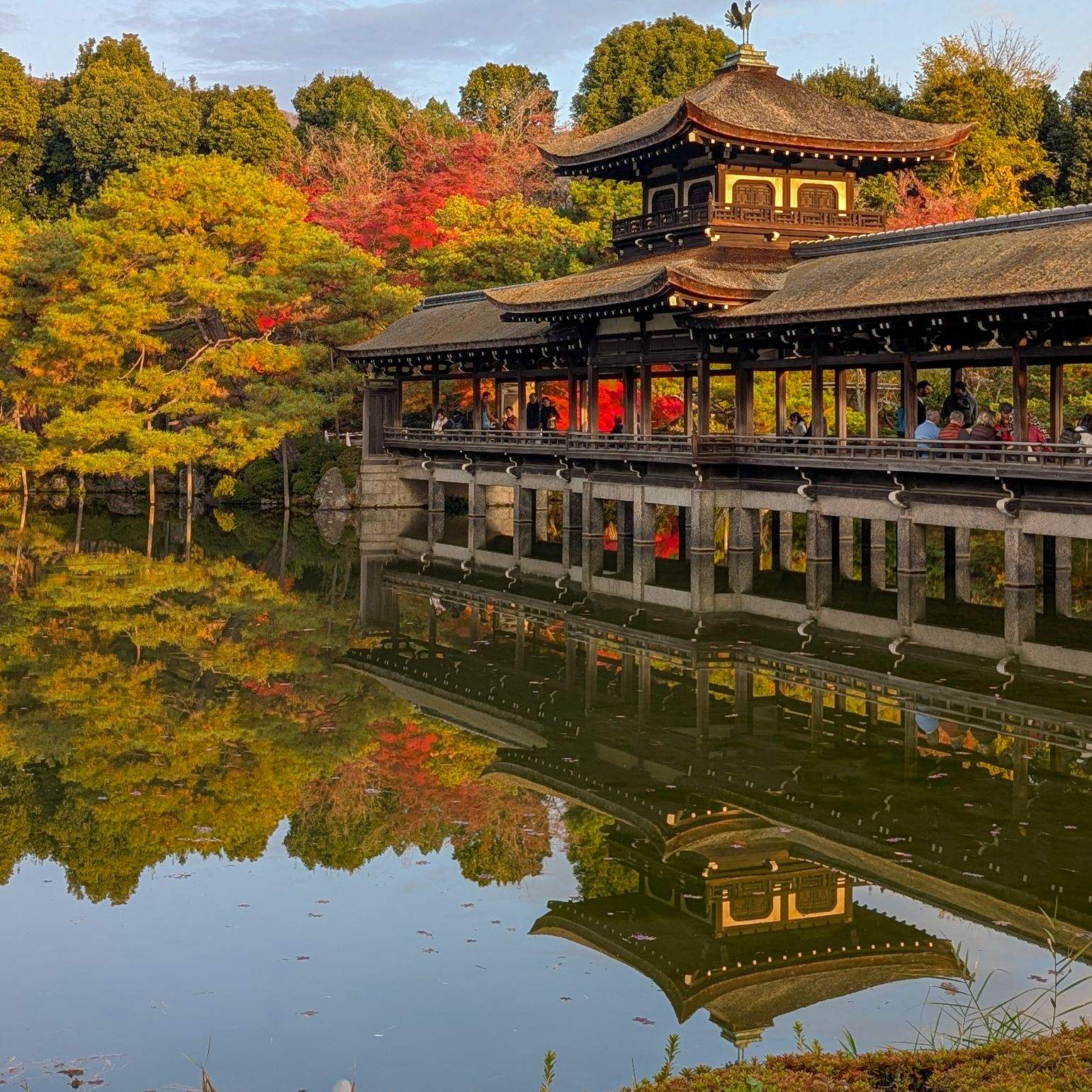 Covered wooden bridge and pagoda at Heian Shrine garden, Kyoto, reflected in a still pond amid autumn foliage.