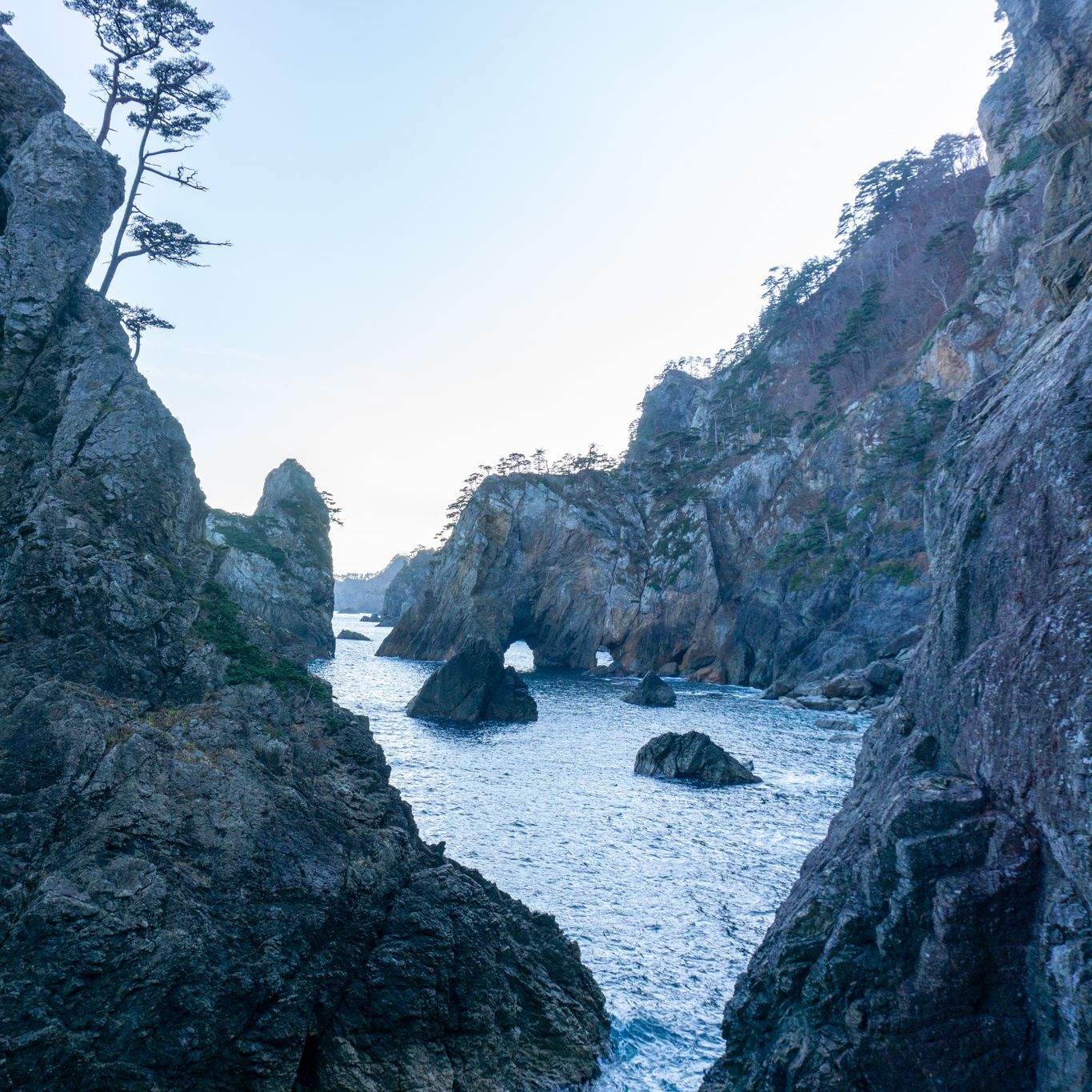 Jagged rock formations framing a narrow sea passage on the Iwate coast, with a natural stone arch and sea stacks visible in the distance.