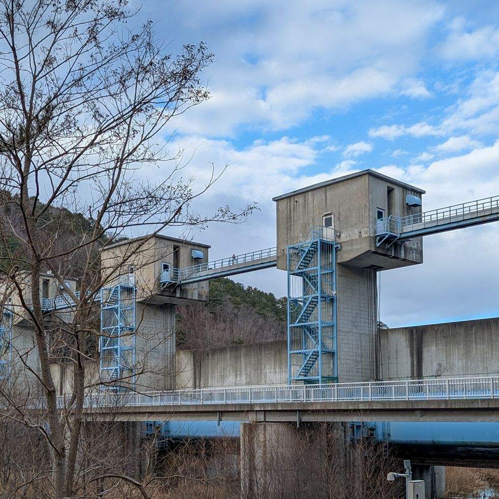 The Fudai floodgate in Iwate, Japan — a large concrete tsunami barrier with blue steel staircases spanning a river inlet.
