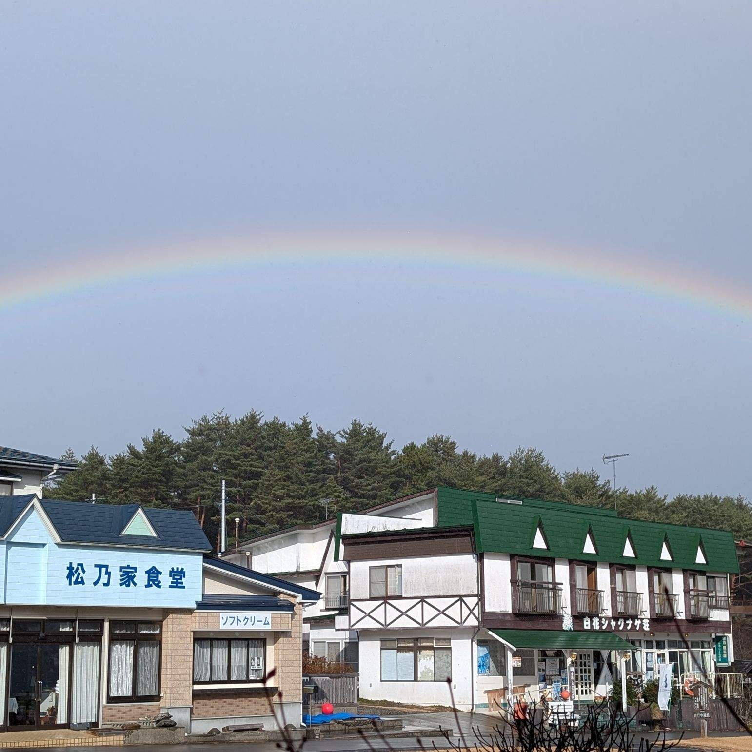 A full rainbow arching over a small coastal village with a restaurant and gift shop, at the end of the Michinoku Coastal Trail, Iwate.