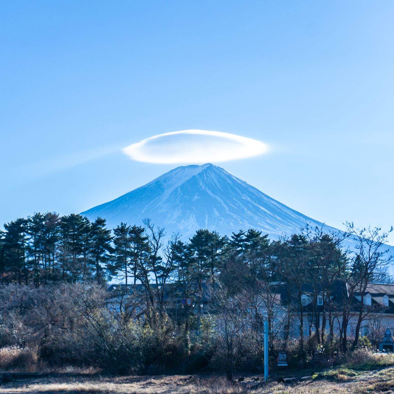Mount Fuji with a lenticular cloud forming a perfect halo above its snow-covered summit against a clear blue sky.