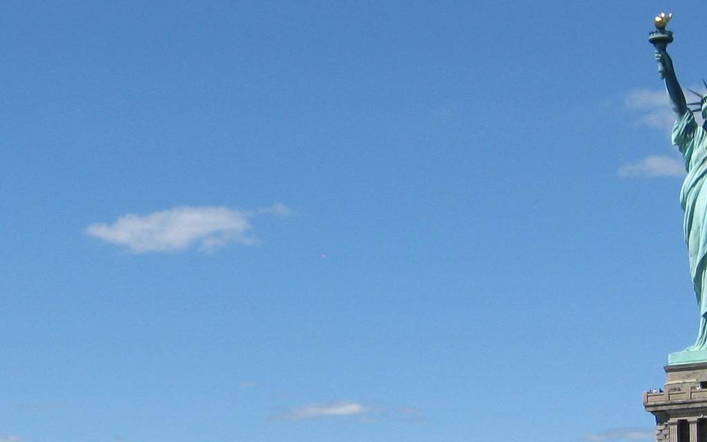 Statue of Liberty seen from a harbor ferry, framed against a deep blue sky with a single dramatic cloud above her.