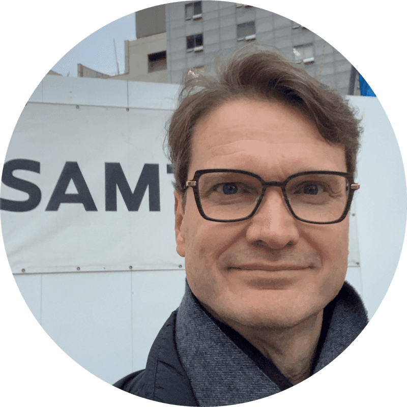 Sam Wilschke in front of a construction hoarding banner reading,"SAM," looking directly at the camera.