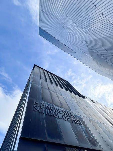 Two tall buildings under blue skies. One says "Manchester School of Art" on the side.