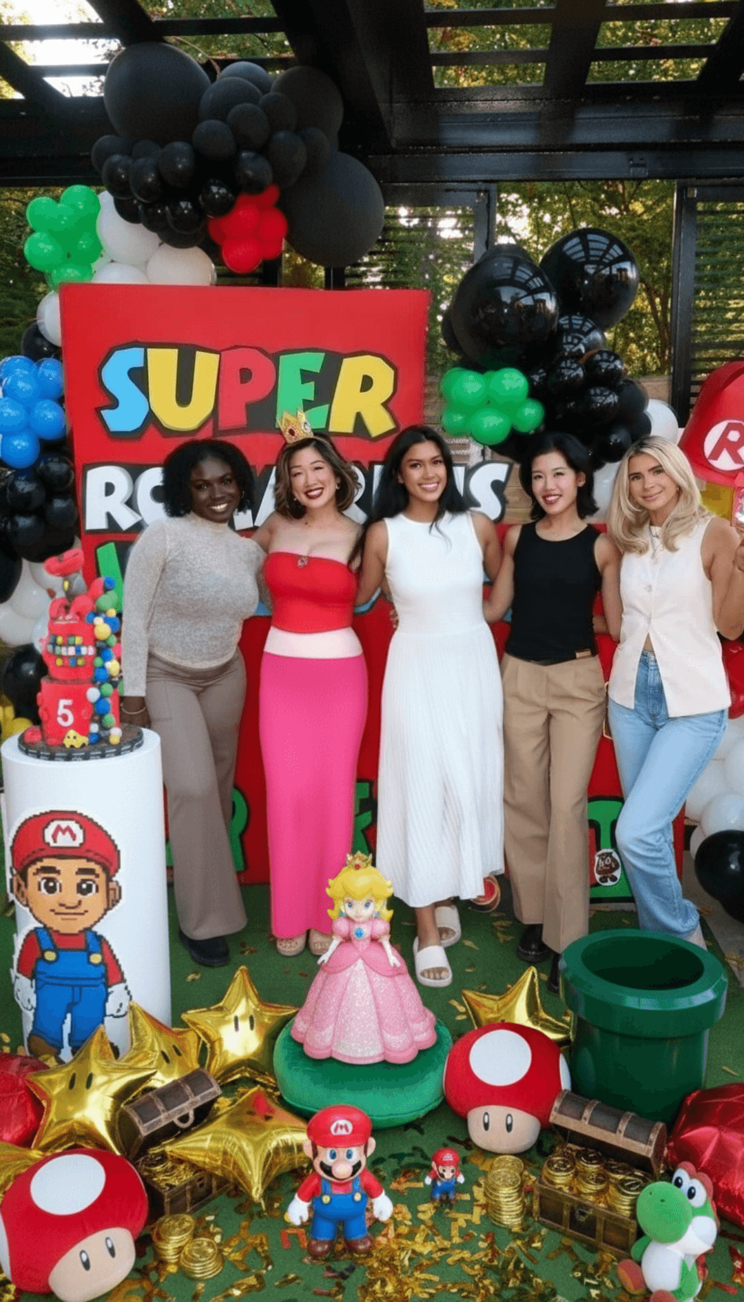 Five women posing with arms around each other at a Super Mario themed birthday party, surrounded by festive decorations on the ground.