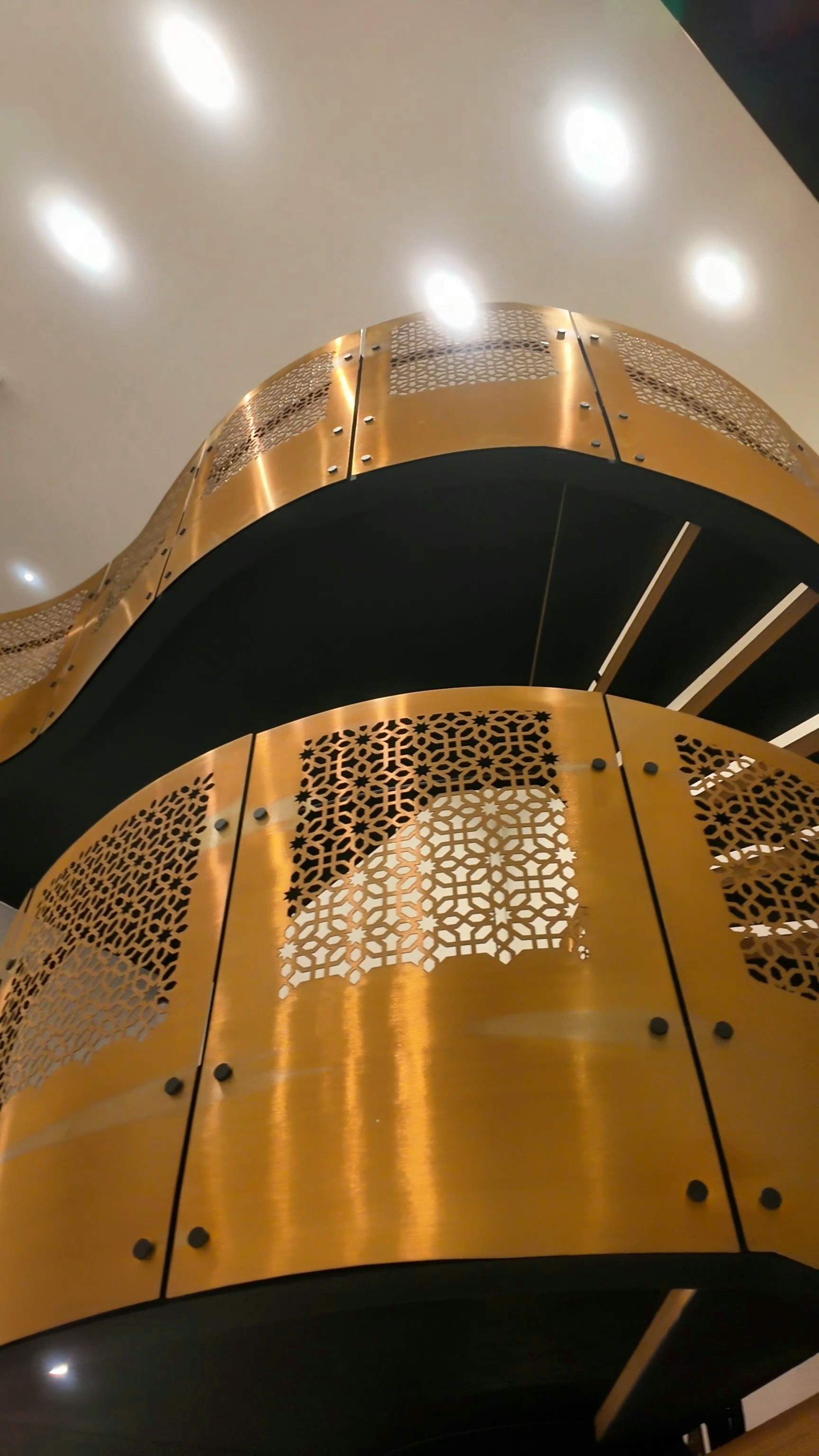 An upward-looking architectural detail shot of Hammam Spa's brushed gold spiral staircase, highlighting the intricate laser-cut metalwork an