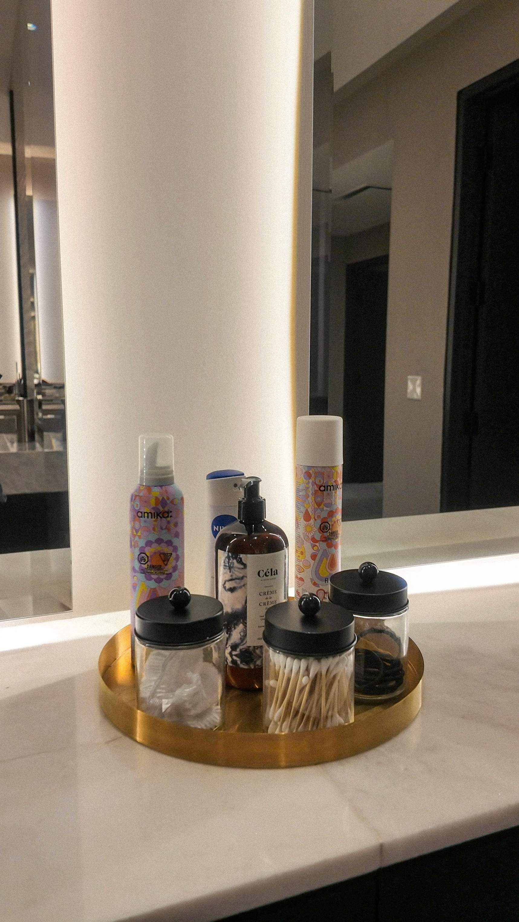 gold tray with Céla Crème de la Crème lotion, Amika hair products, cotton pads, and Q-tips on a marble vanity in Hammam Spa's luxurious chan