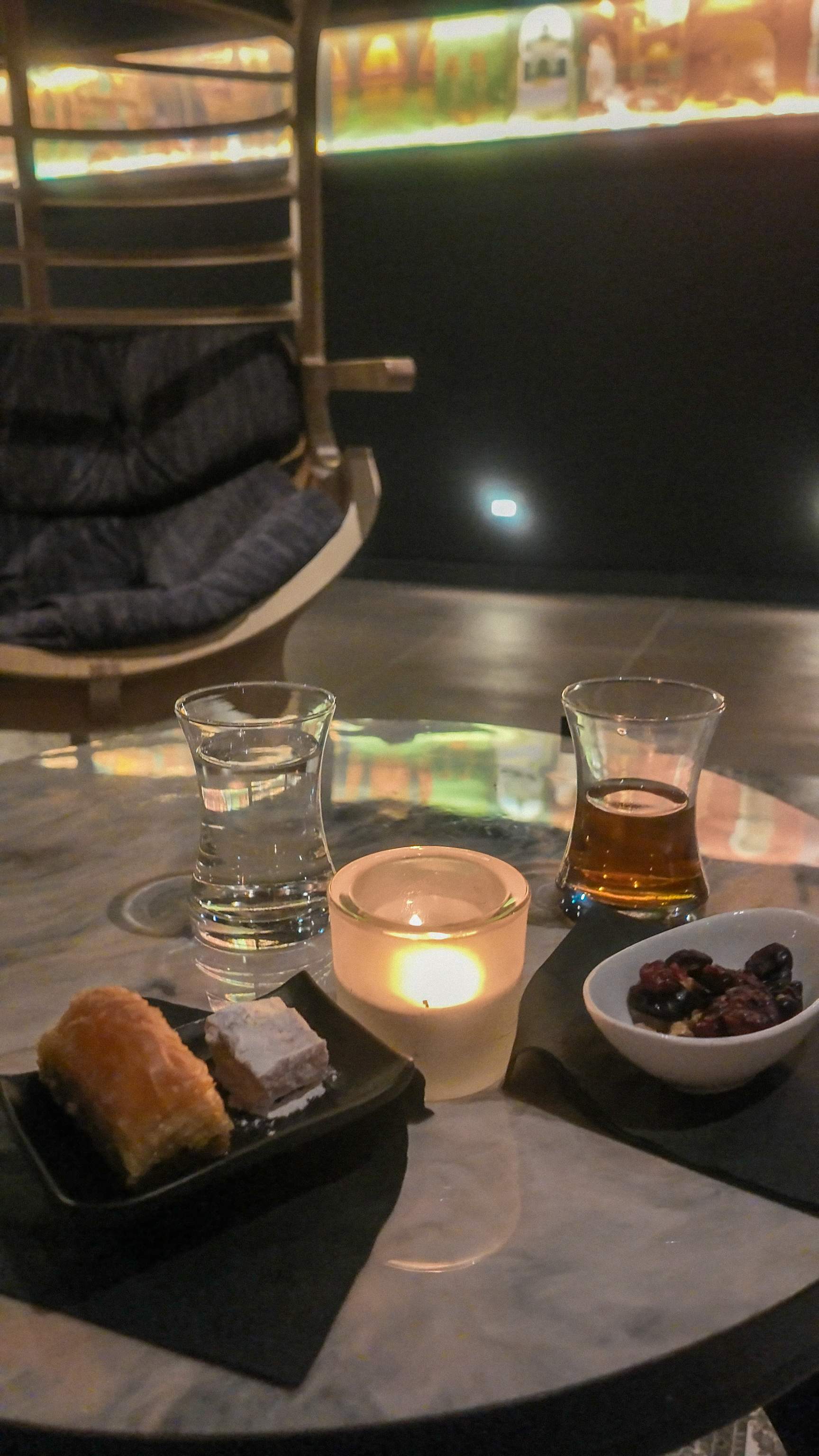 Close-up of a marble table in Hammam Spa's tea lounge, showing warm tea, baklava, Turkish delight, dried cranberries, water, and a lit candl