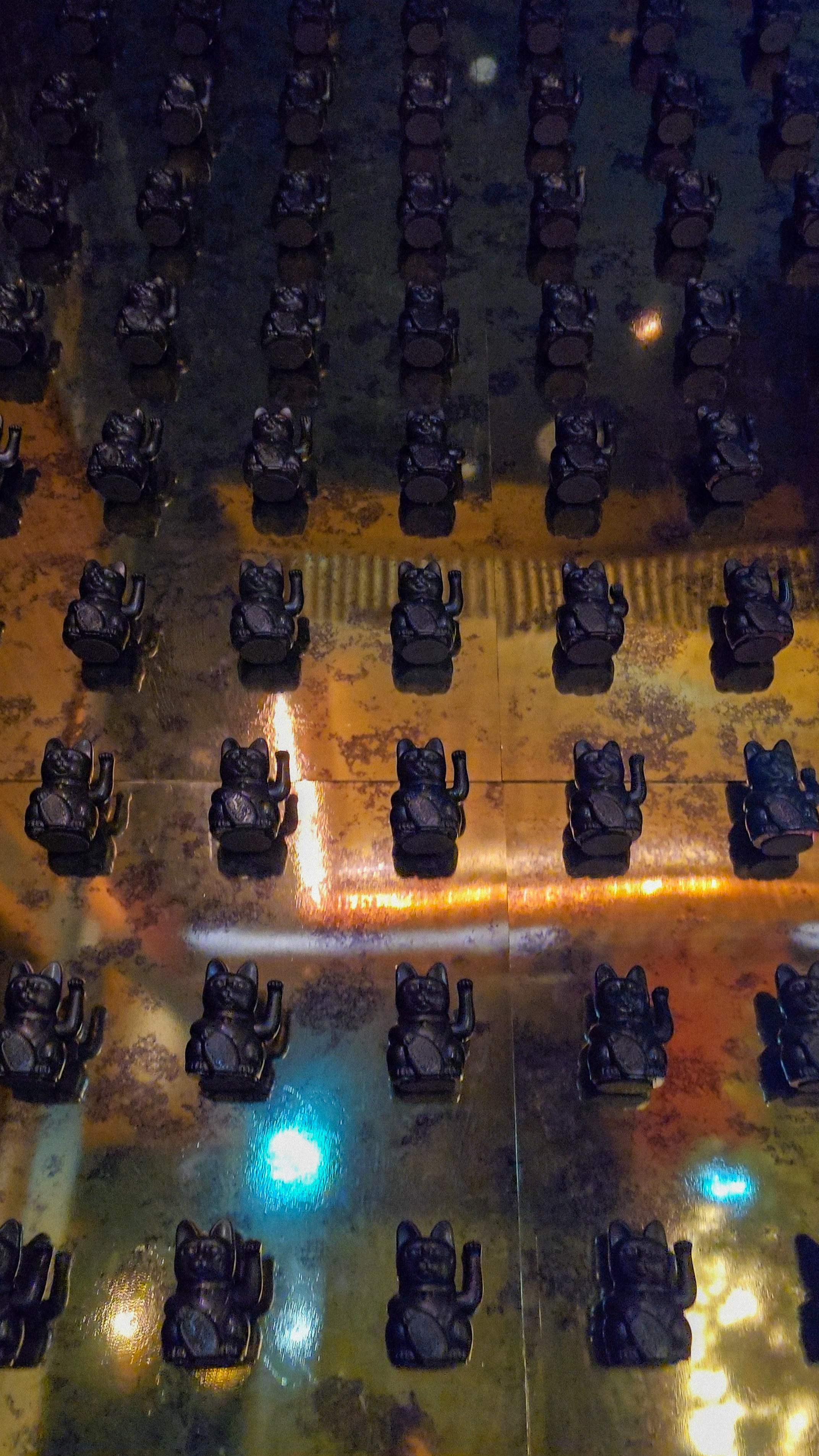 Decorative wall featuring rows of black waving Lucky Cats (Maneki-neko) on a gold background at Pears Restaurant.