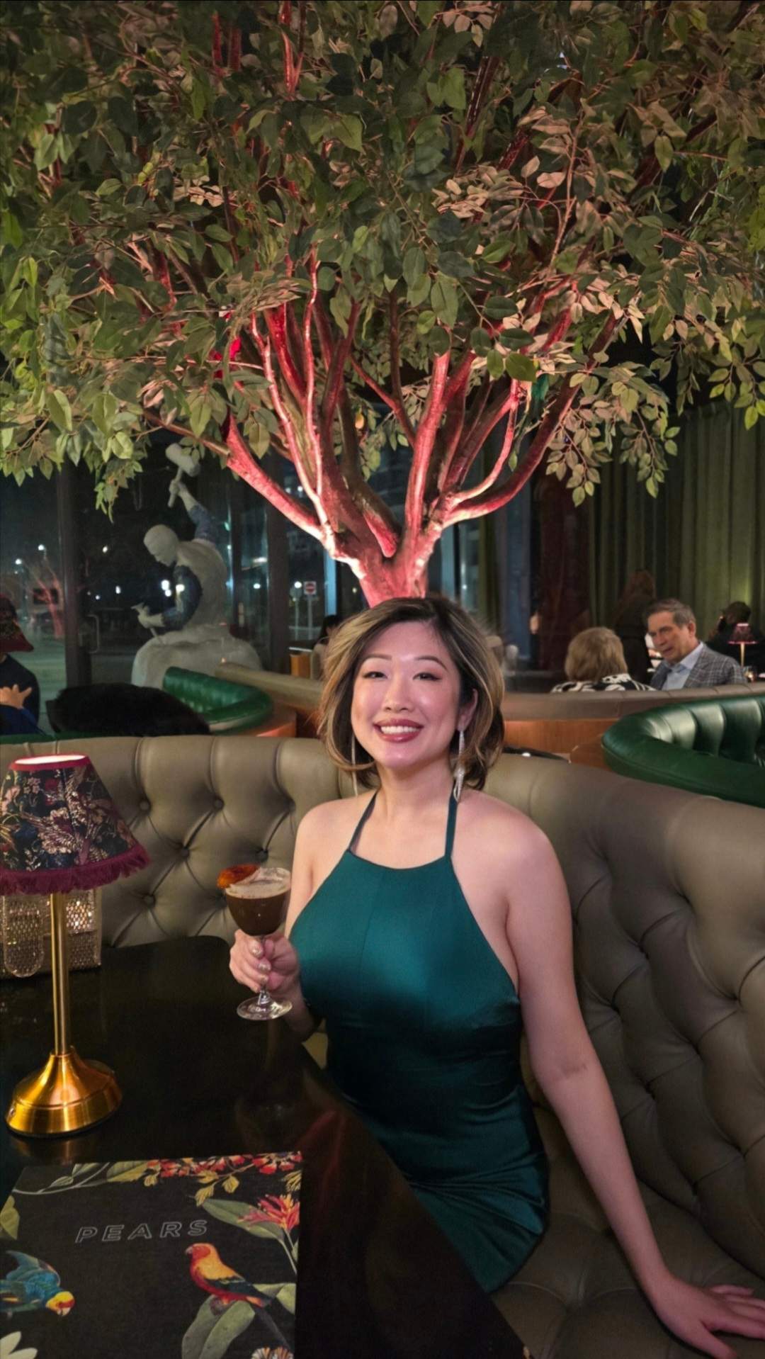 Guest holding a signature cocktail while sitting in a green velvet booth at Pears Restaurant in Downtown Markham.