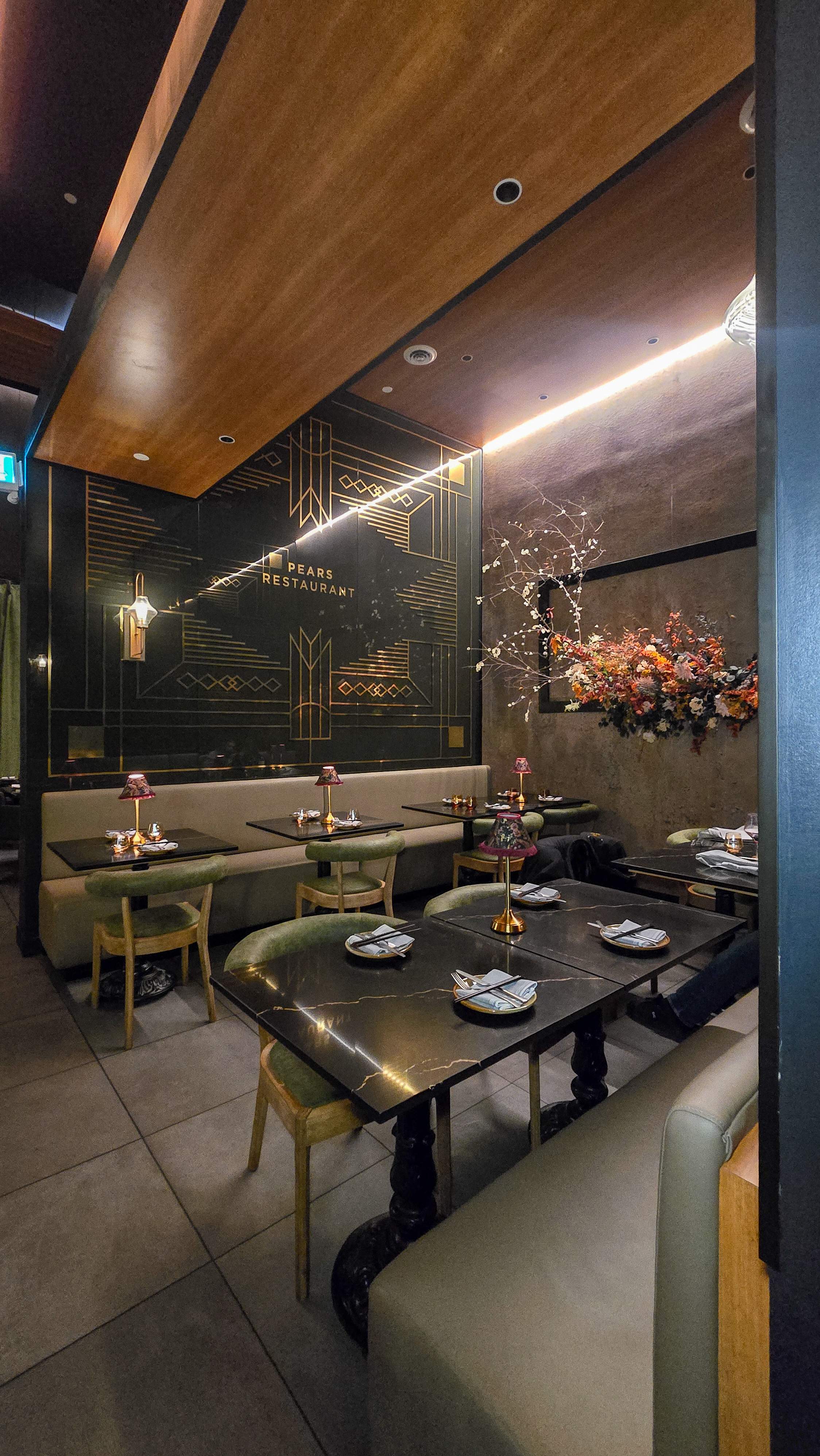 Interior of Pears Restaurant Markham featuring gold Art Deco wall designs, green velvet booths, and moody ambient lighting.