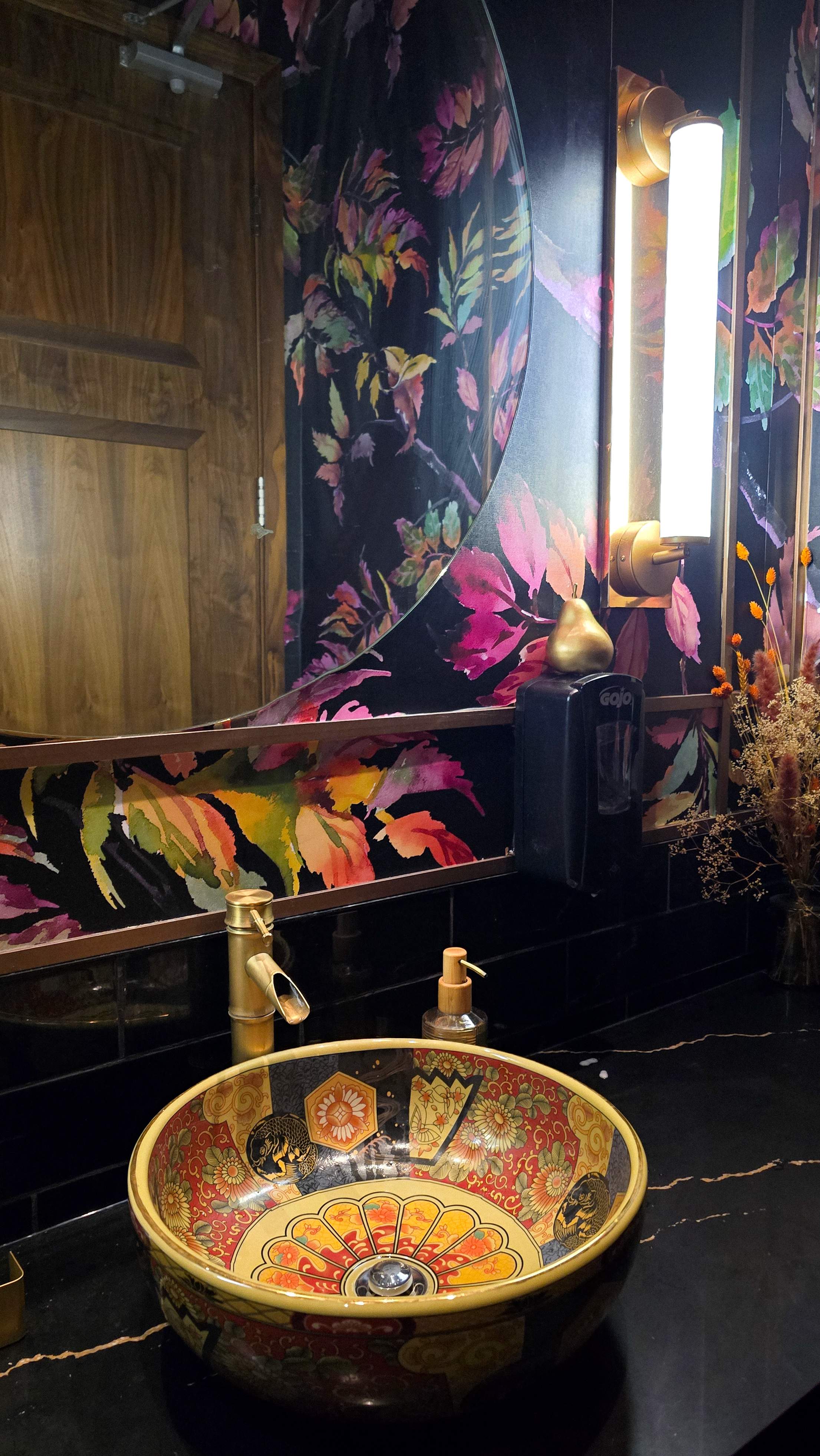 Luxurious bathroom design at Pears Restaurant featuring a colorful Asian-patterned ceramic sink, gold bamboo faucet,  moody floral wallpaper