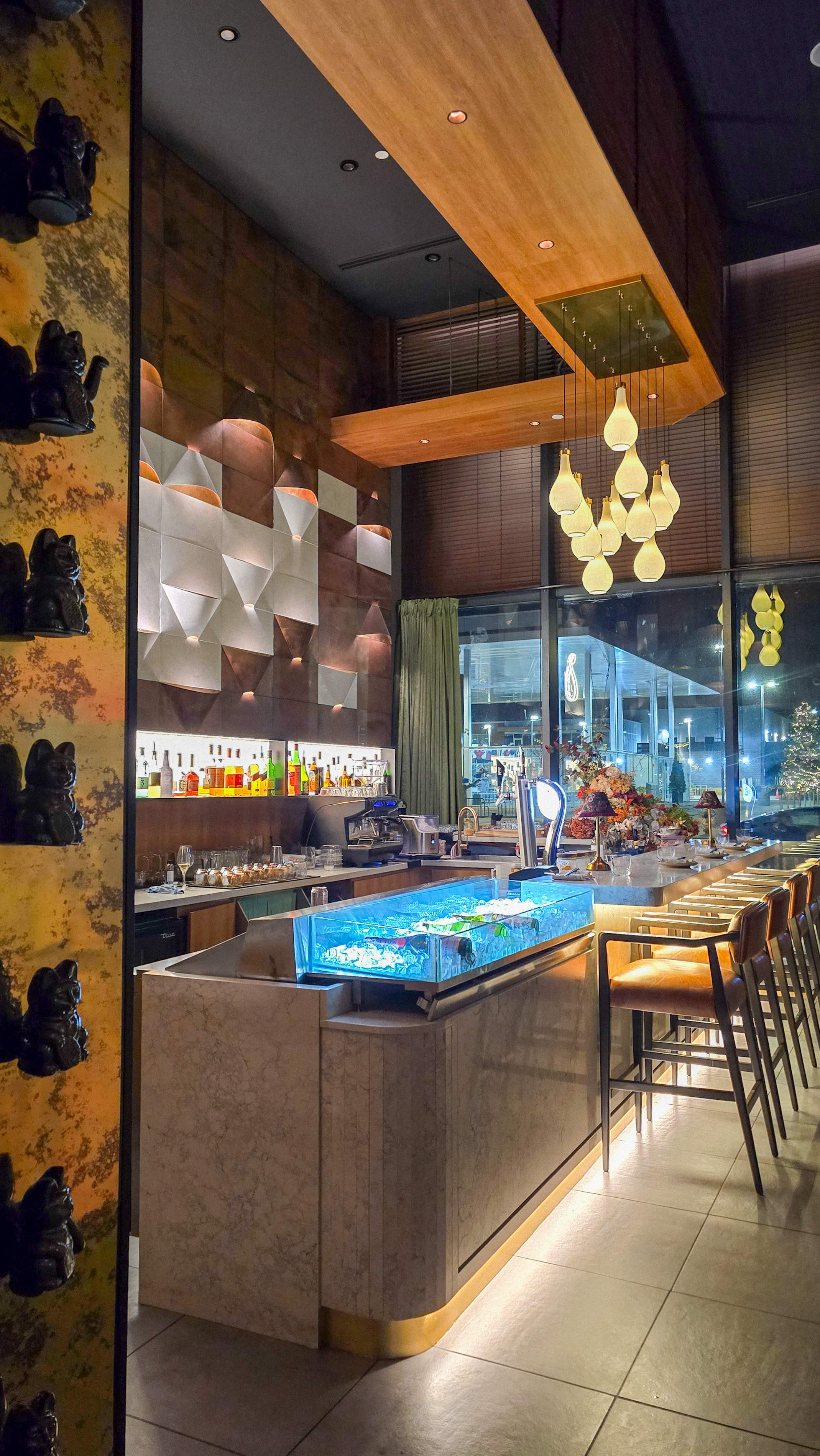 Modern bar area at Pears Restaurant featuring pear-shaped pendant lights, a fresh raw bar display, and a signature gold wall filled with bla