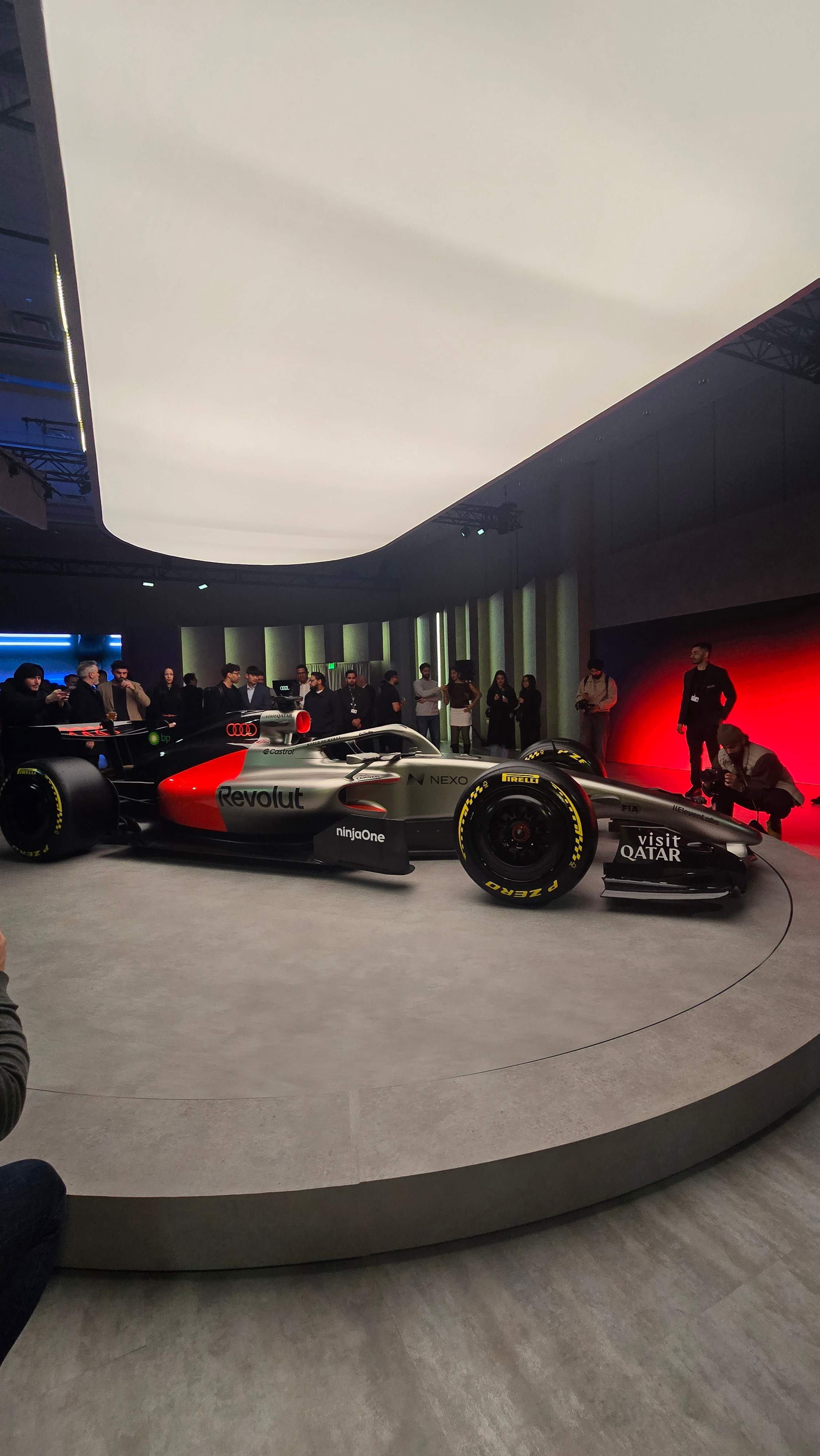 Silver, black, red Audi R26 Formula 1 concept car displayed on a circular platform under cinematic lighting at  Audi Haus 2026 Cias2026