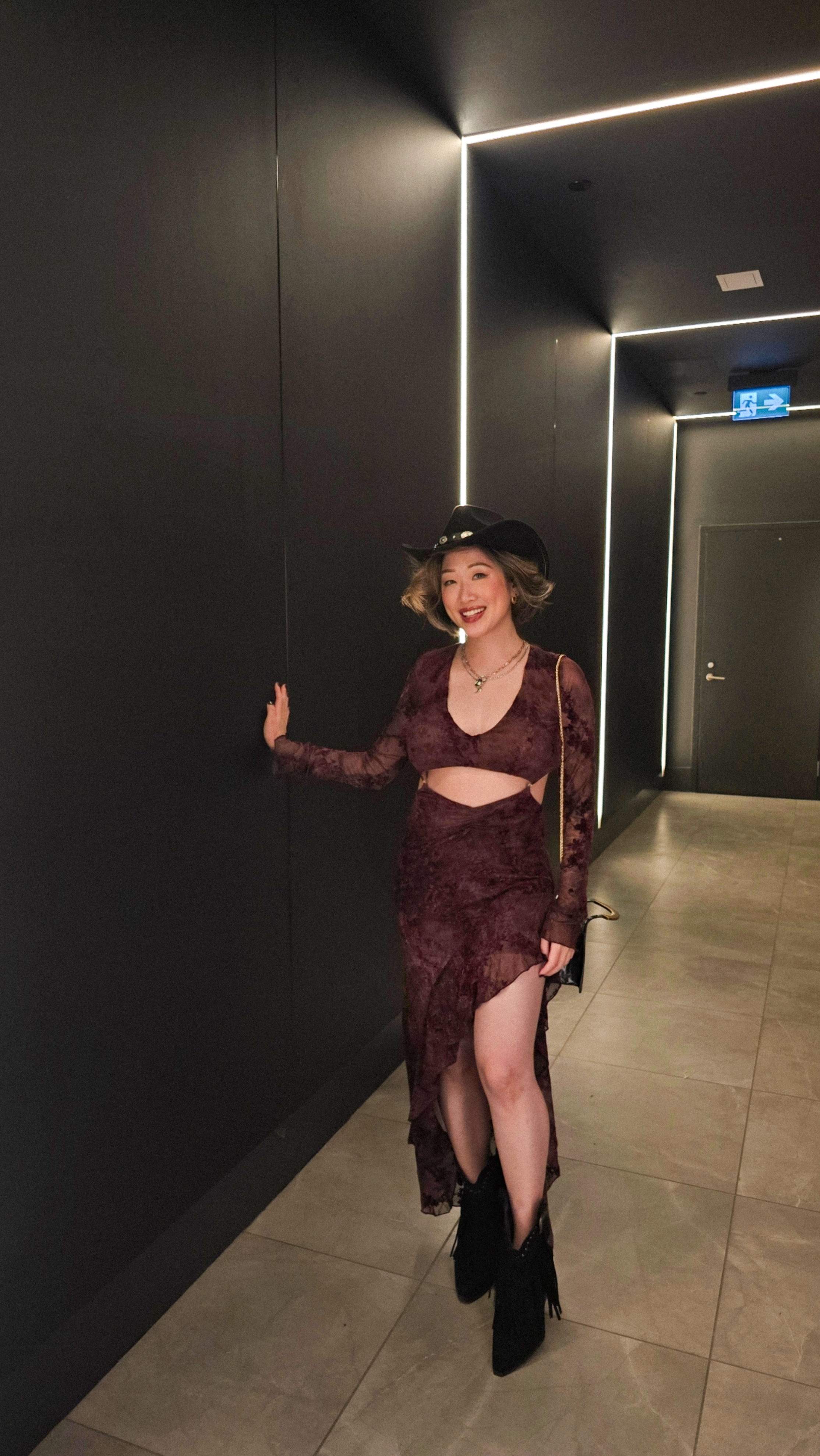 Full body outfit photo wearing a black cowboy hat, fringe boots, and a burgundy maxi dress in a modern hallway at HISTORY Toronto! 🤍
