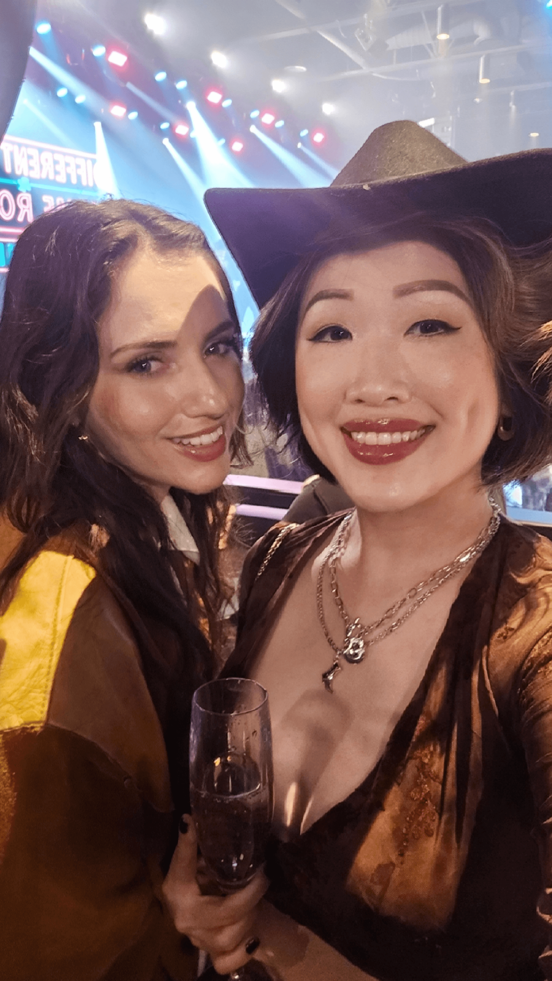 Courtney and I smiling with cocktails in our private VIP booth with the concert stage glowing behind us during our Toronto girls night!