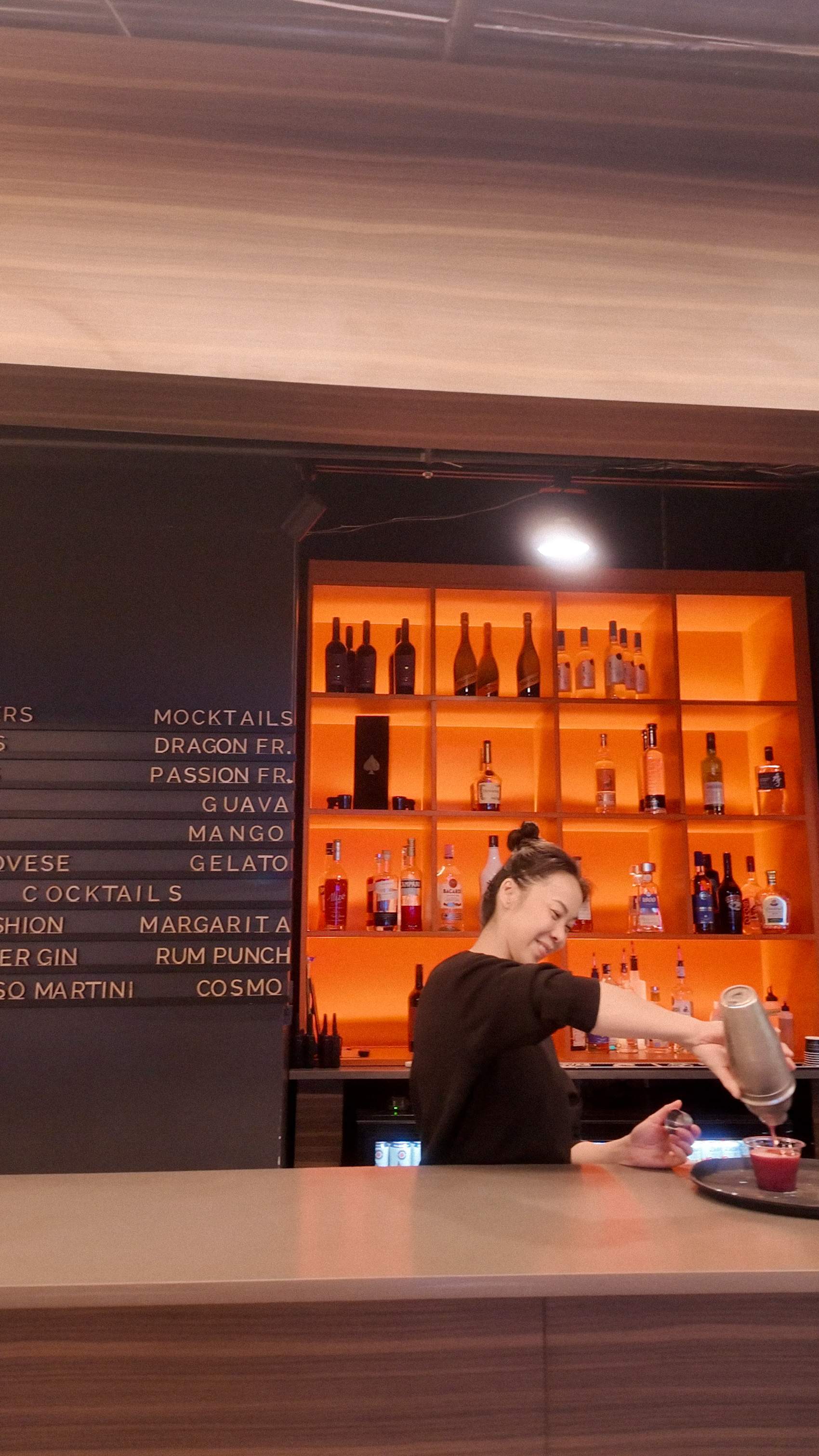 bartender pouring a custom cocktail at the fully stocked, warmly lit wooden paint bar inside Paint Cabin in Toronto. 