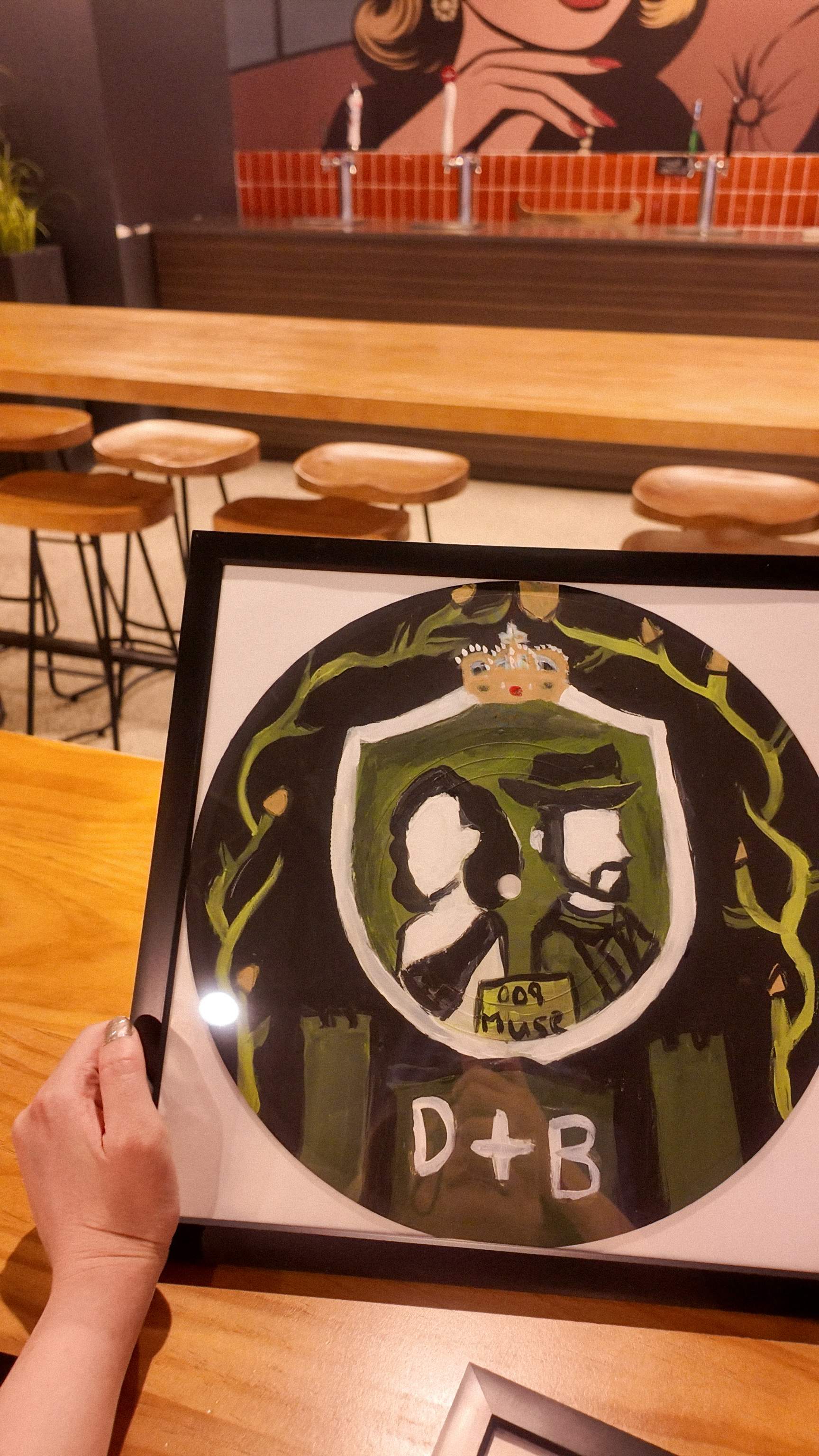 Close-up of a framed James Bond themed painted vinyl record resting on a wooden table inside the Paint Cabin studio. 