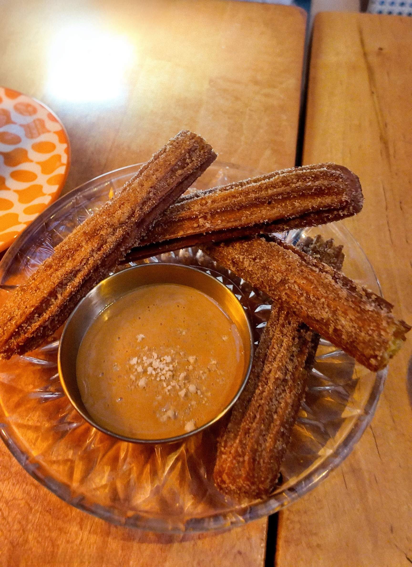Freshly fried churros with cinnamon sugar are arranged around dulce de leche on a vintage glass plate.