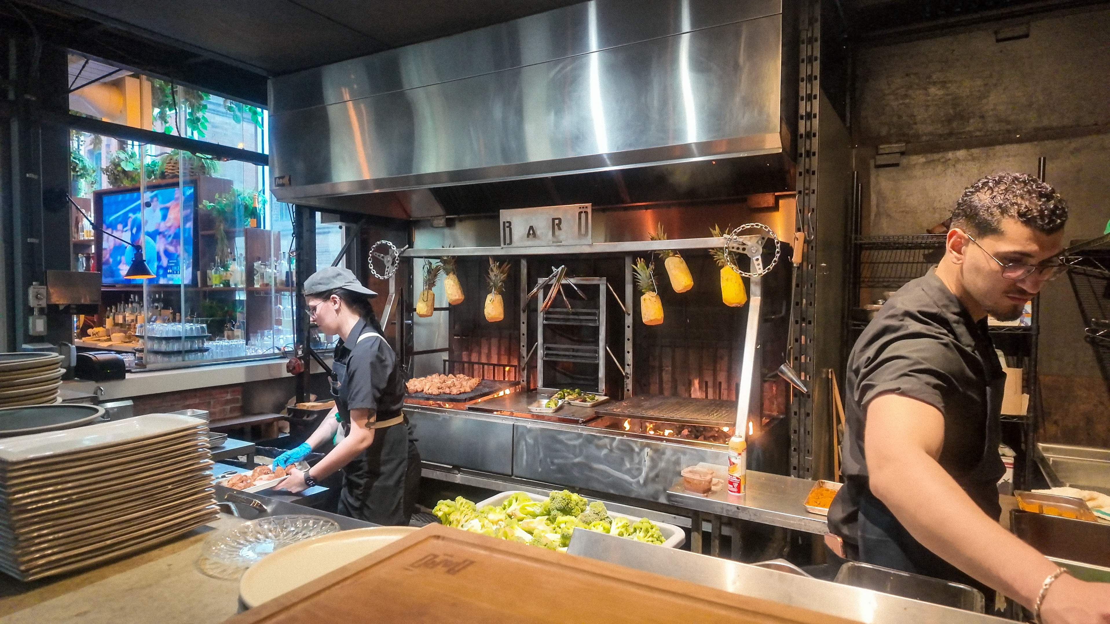 View of the open kitchen at Baro Toronto on King West, showing chefs at prep stations with hanging pineapples