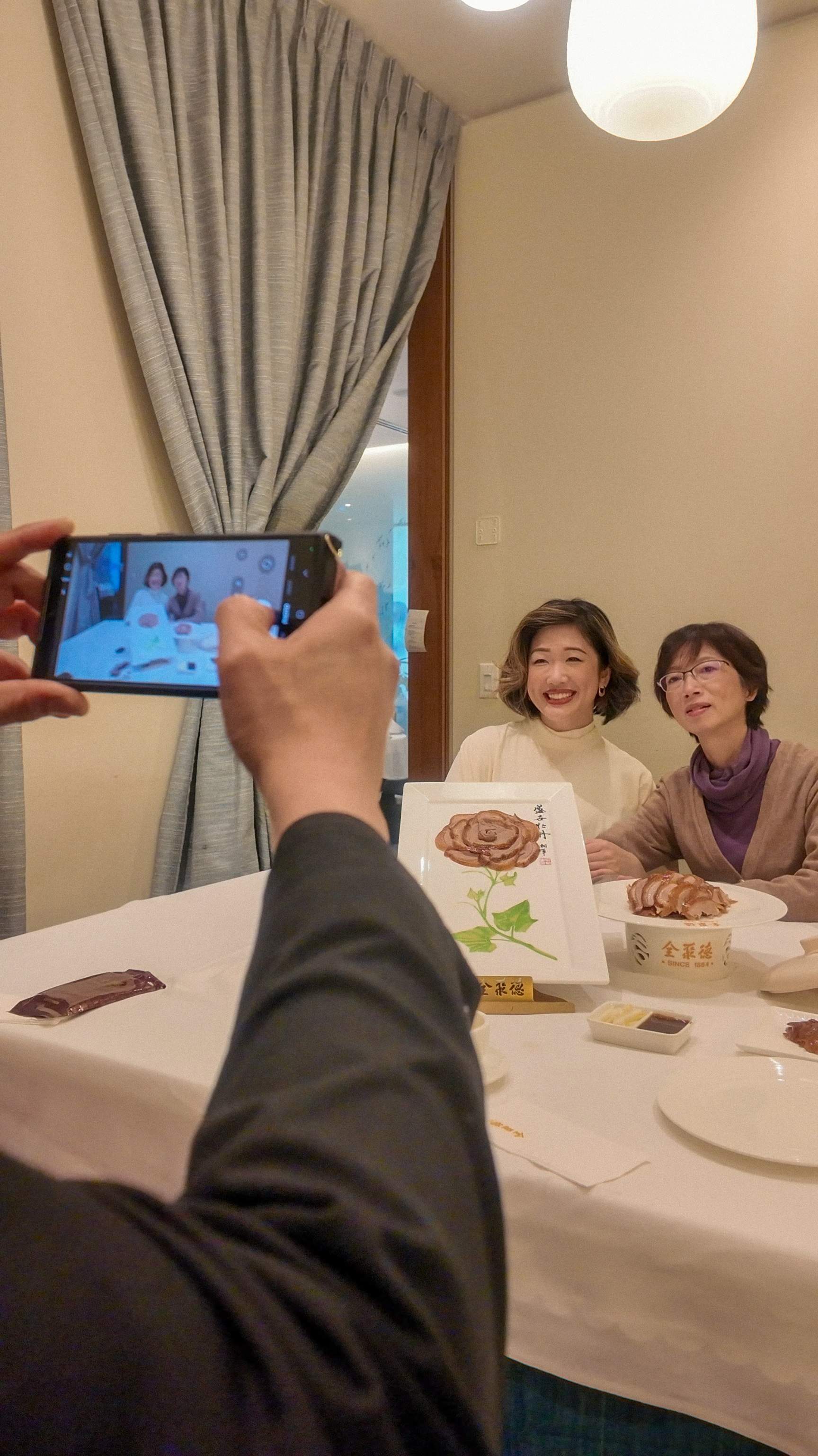 Manager at QJD Peking Duck Markham taking photo of mother and daughter smiling at private dining table with Peony Duck presentation plate an