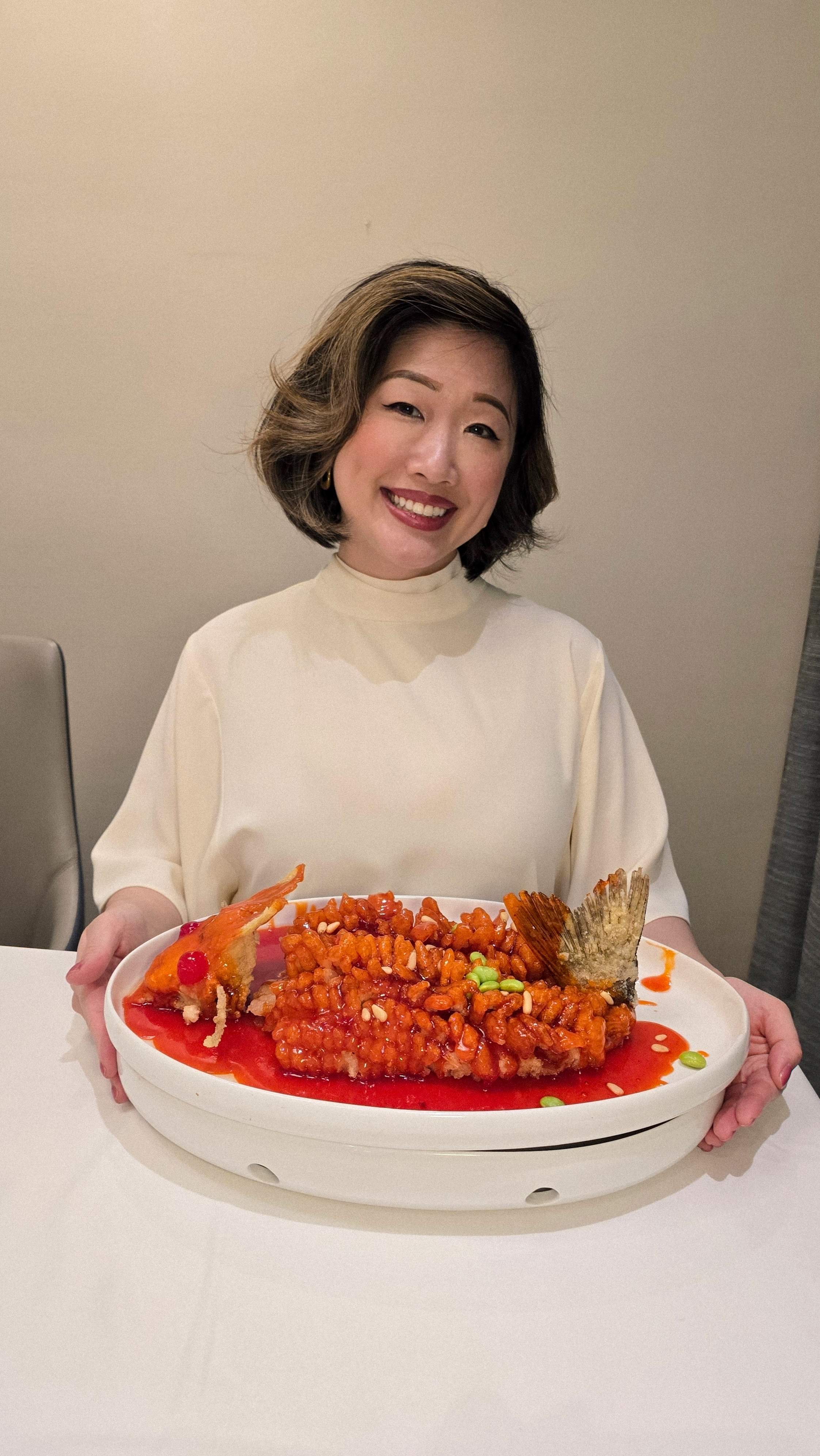Woman smiling and holding large plate of QJD Markham Signature Crispy Fish with Sweet and Sour Sauce in private dining room best Chinese res