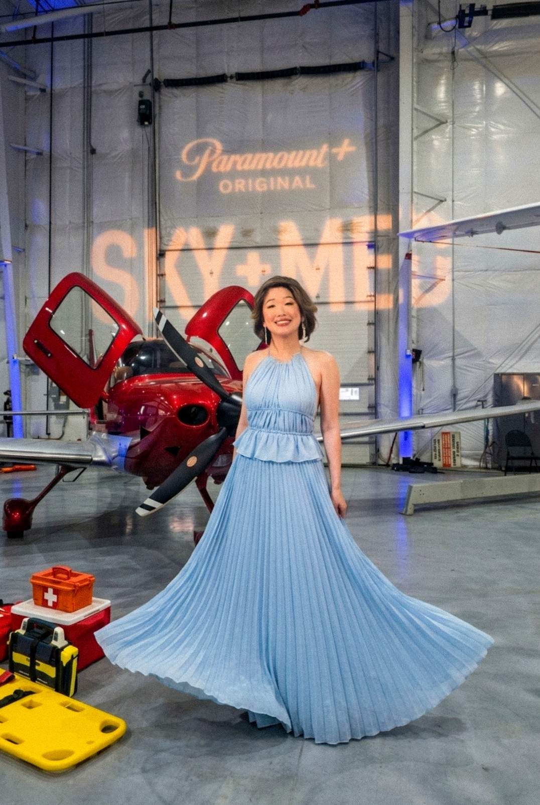 Digital creator Betty Lam wearing a stunning black lace cutout gown posing in front of a sleek black and red Cirrus aircraft. The iconic dow