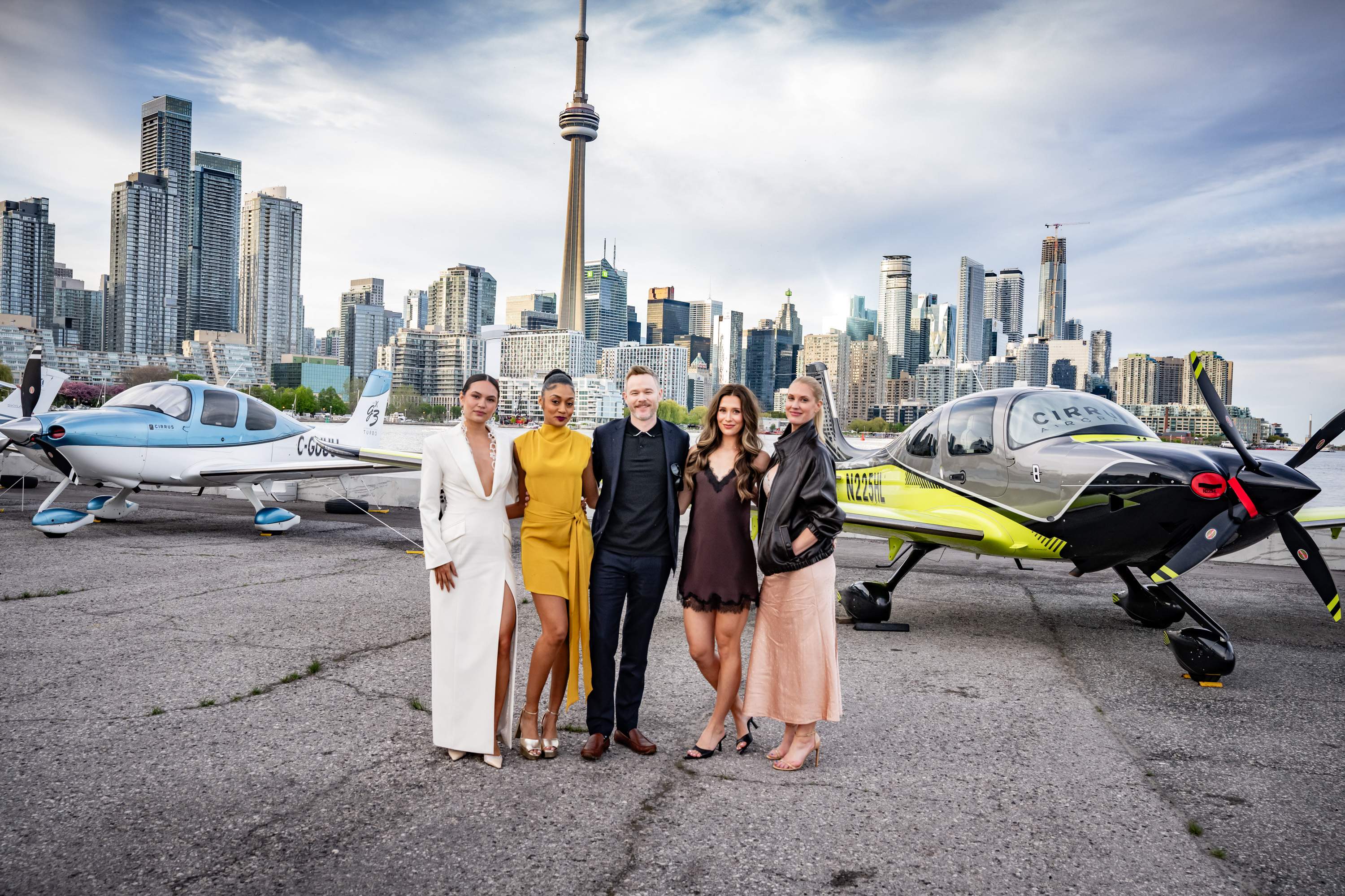Five cast members of the Paramount Plus series SkyMed posing together on the tarmac at Billy Bishop Airport. They are standing between two p