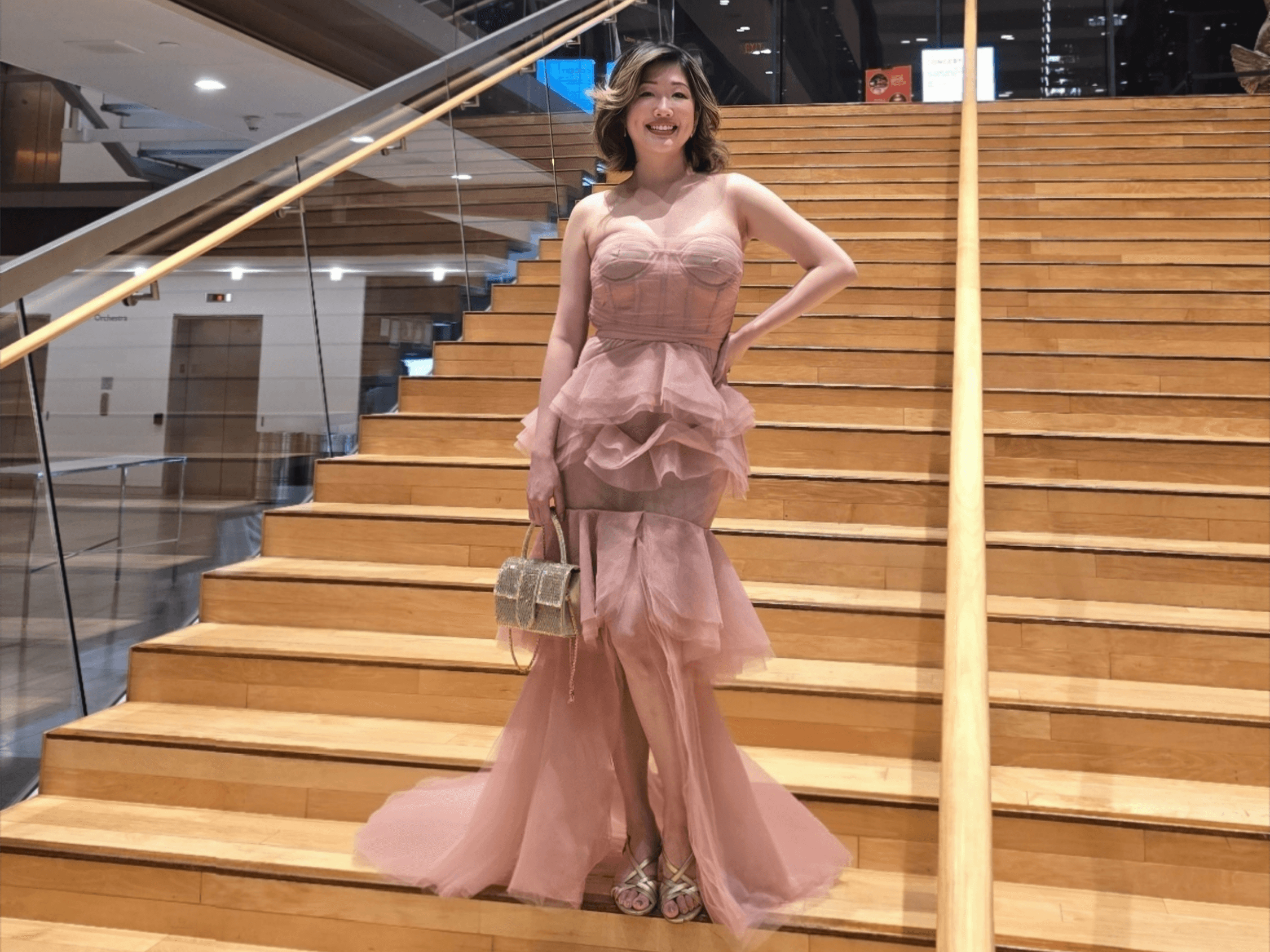 Luxury fashion blogger posing in a pink ruffled gown on the grand wooden staircase of the Four Seasons Centre for Performing Arts, Toronto