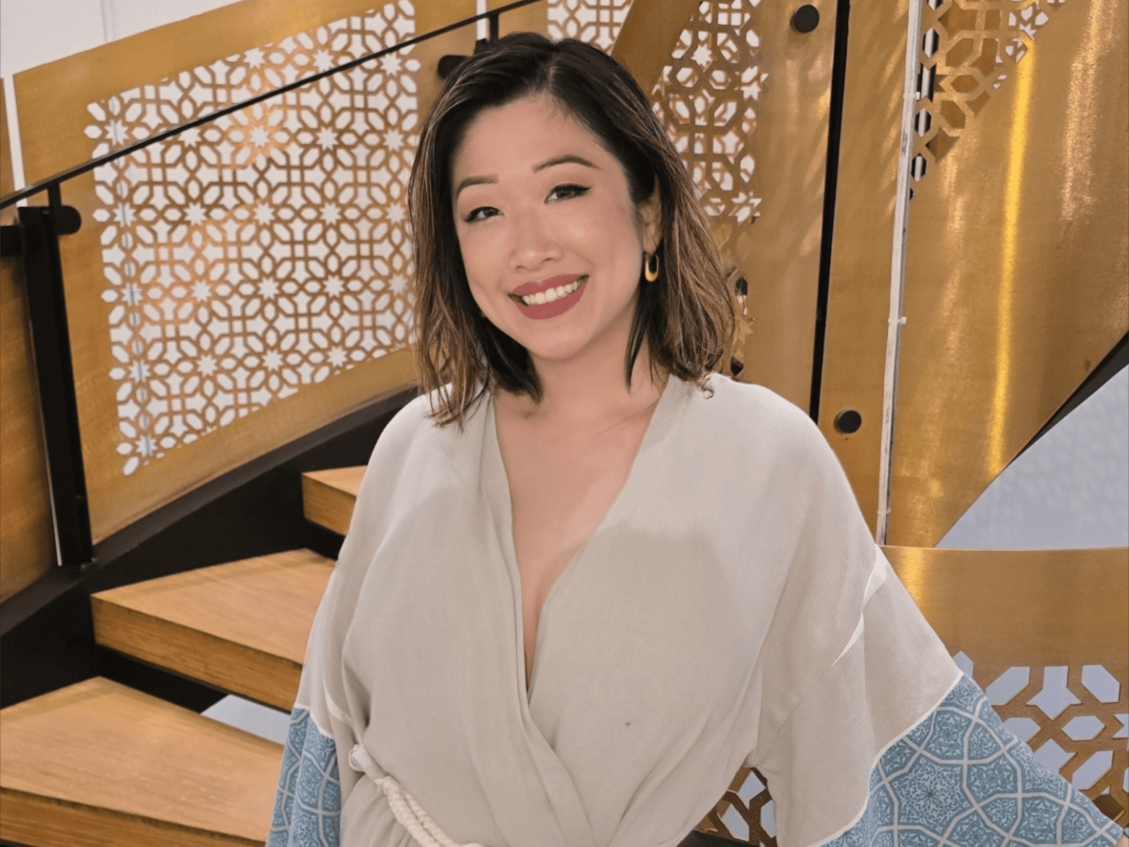 A woman in a patterned spa robe descending the iconic golden spiral staircase at Hammam Spa in Toronto, showcasing the spa's luxurious Easte