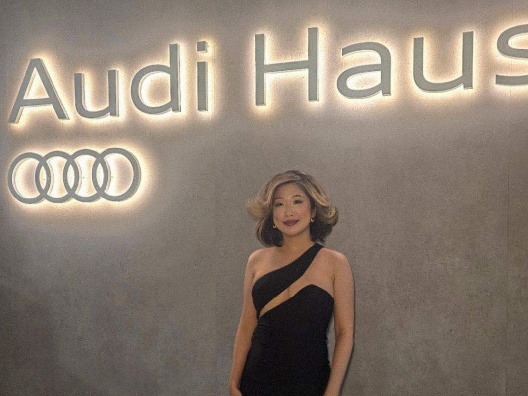 A fashion and lifestyle creator wearing an elegant one-shoulder black gown, posing confidently at the VIP Opening Night of Audi Haus during 