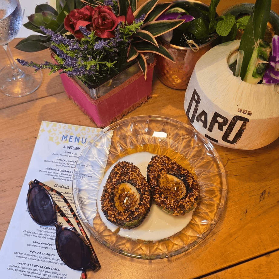 Top-down view of grilled avocado with a tajin and sesame crust on a clear glass plate with sunglasses.