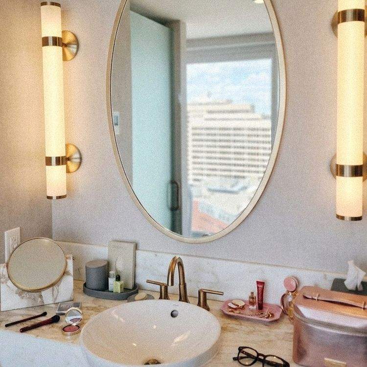 Elegant marble bathroom vanity at Sutton Place Hotel Halifax featuring an oval mirror, modern lighting, and makeup on the counter.