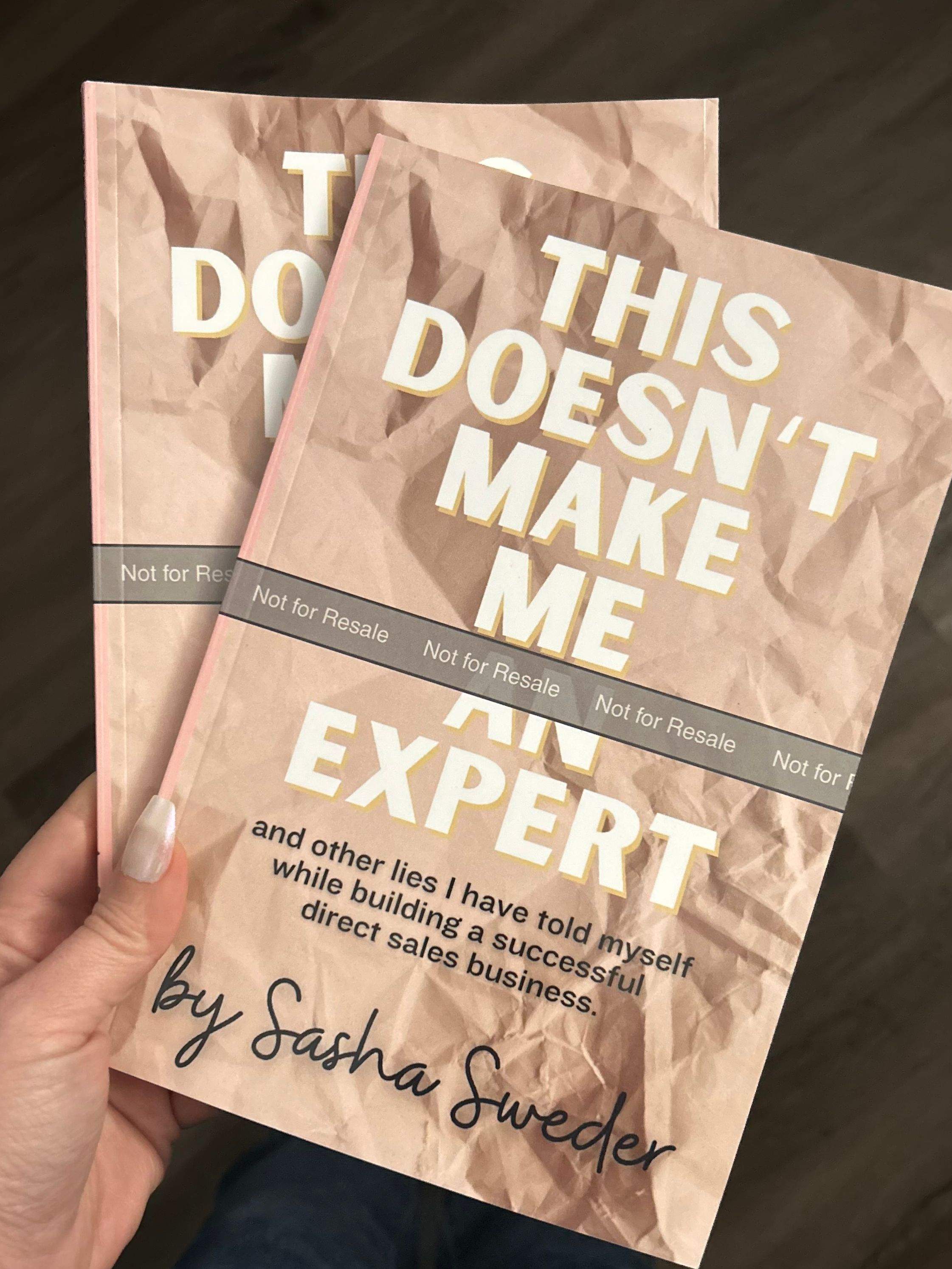 Sasha Sweder holding two printed proof copies of This Doesn’t Make Me an Expert, with tan covers and a Not for Resale band.